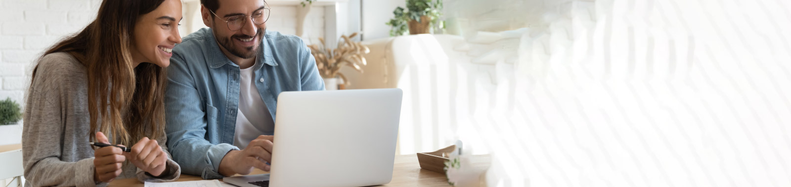 A young couple explore content on a computer at their dining table.