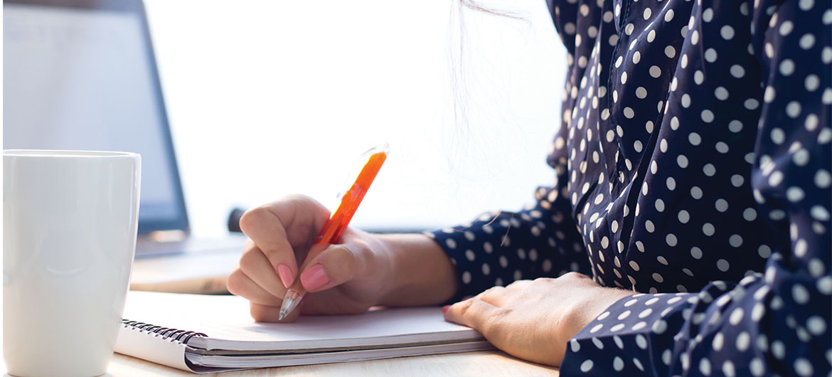 Woman writing notes next to a computer