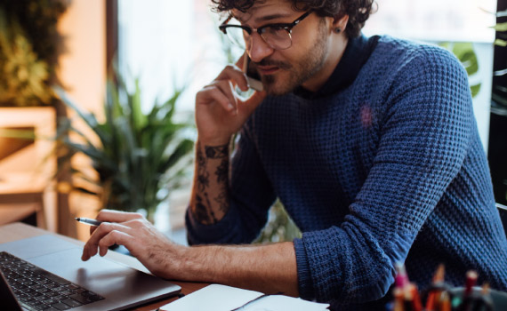 Business man holds a phone to his ear as he looks at his computer.