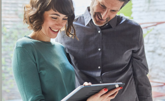 Business woman holds a tablet she is working on while a male coworker watches.